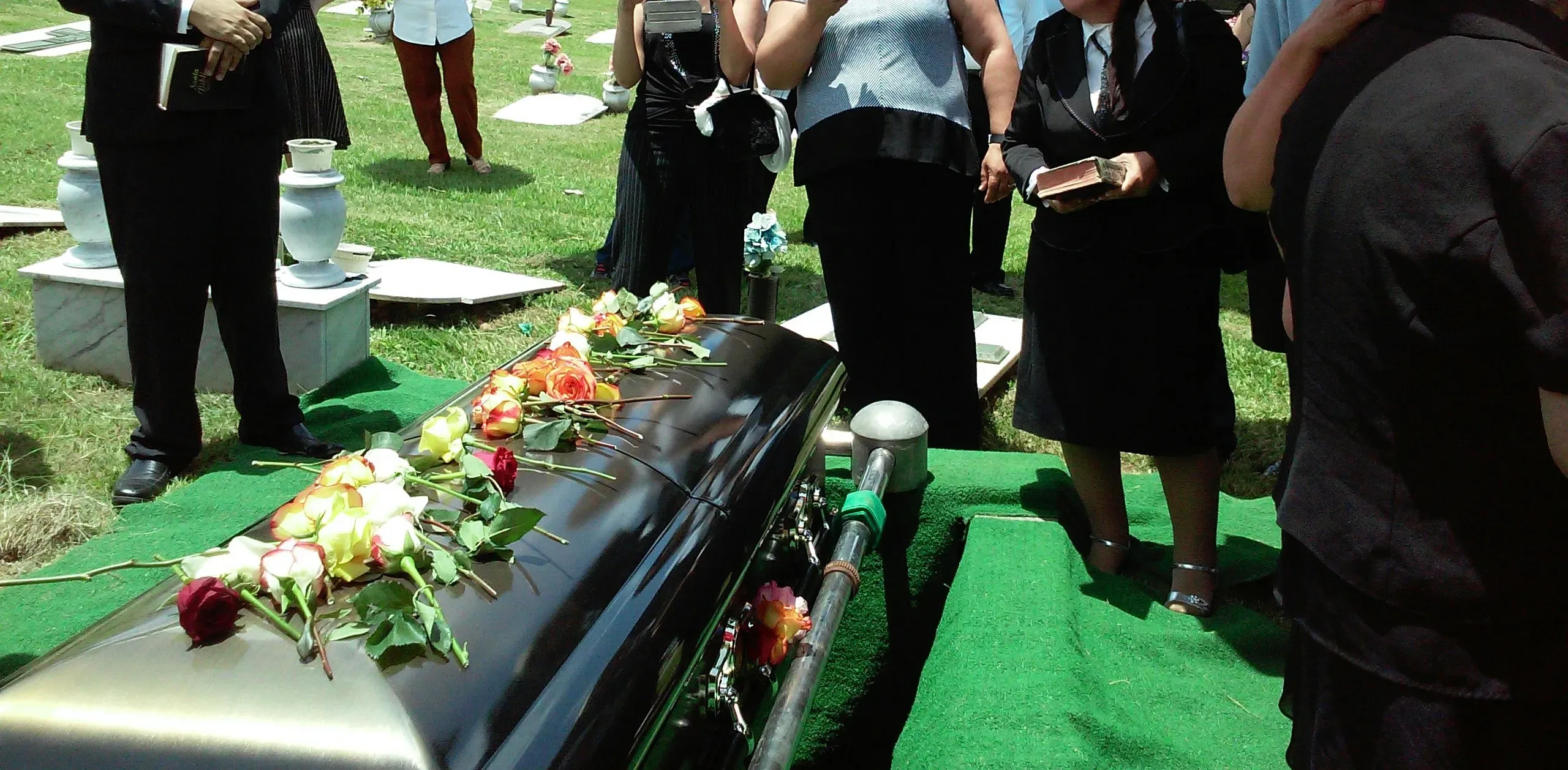 Cérémonie d'inhumation au cimetière autour d'un cercueil recouvert de fleurs.