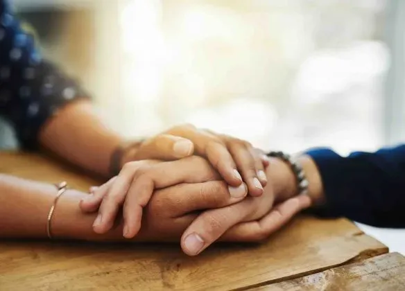 Mains d'un conseiller funéraire tenant les mains d'un client endeuillé en soutien.