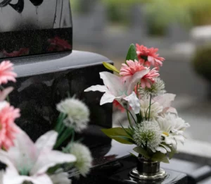 Bouquet de fleurs artificielles roses et blanches sur une tombe en marbre noir.