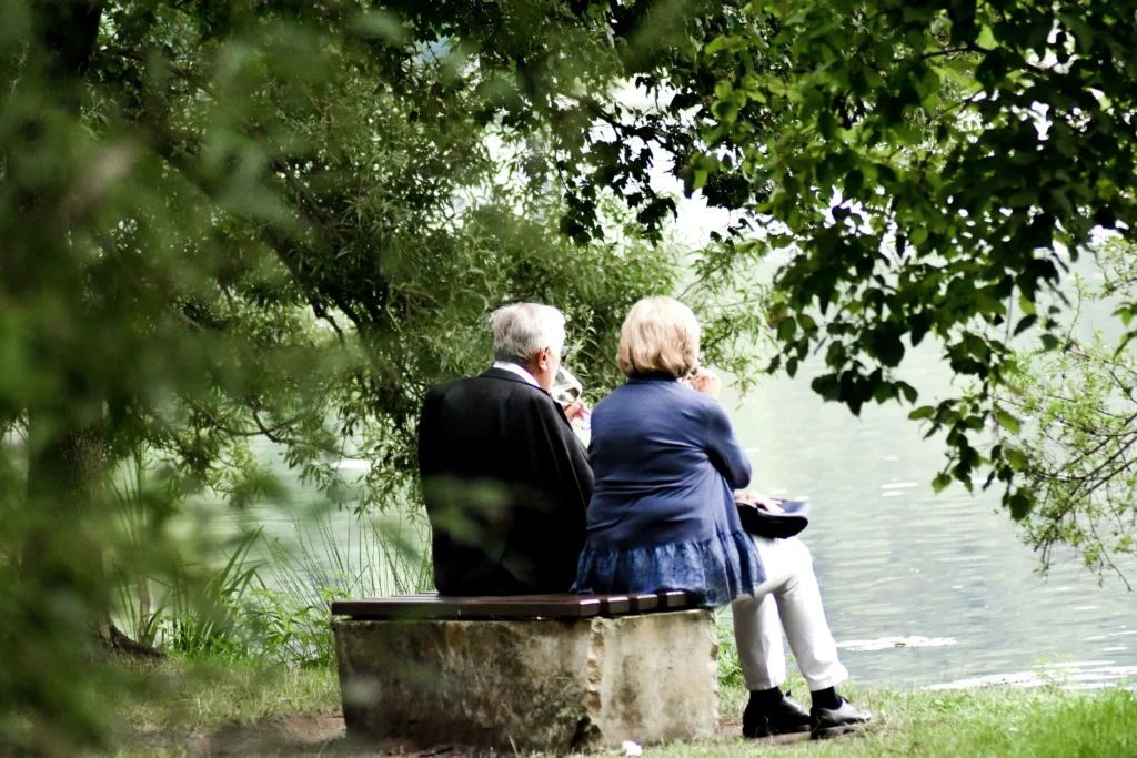 Un couple de seniors se détend sur un banc face à un lac paisible.